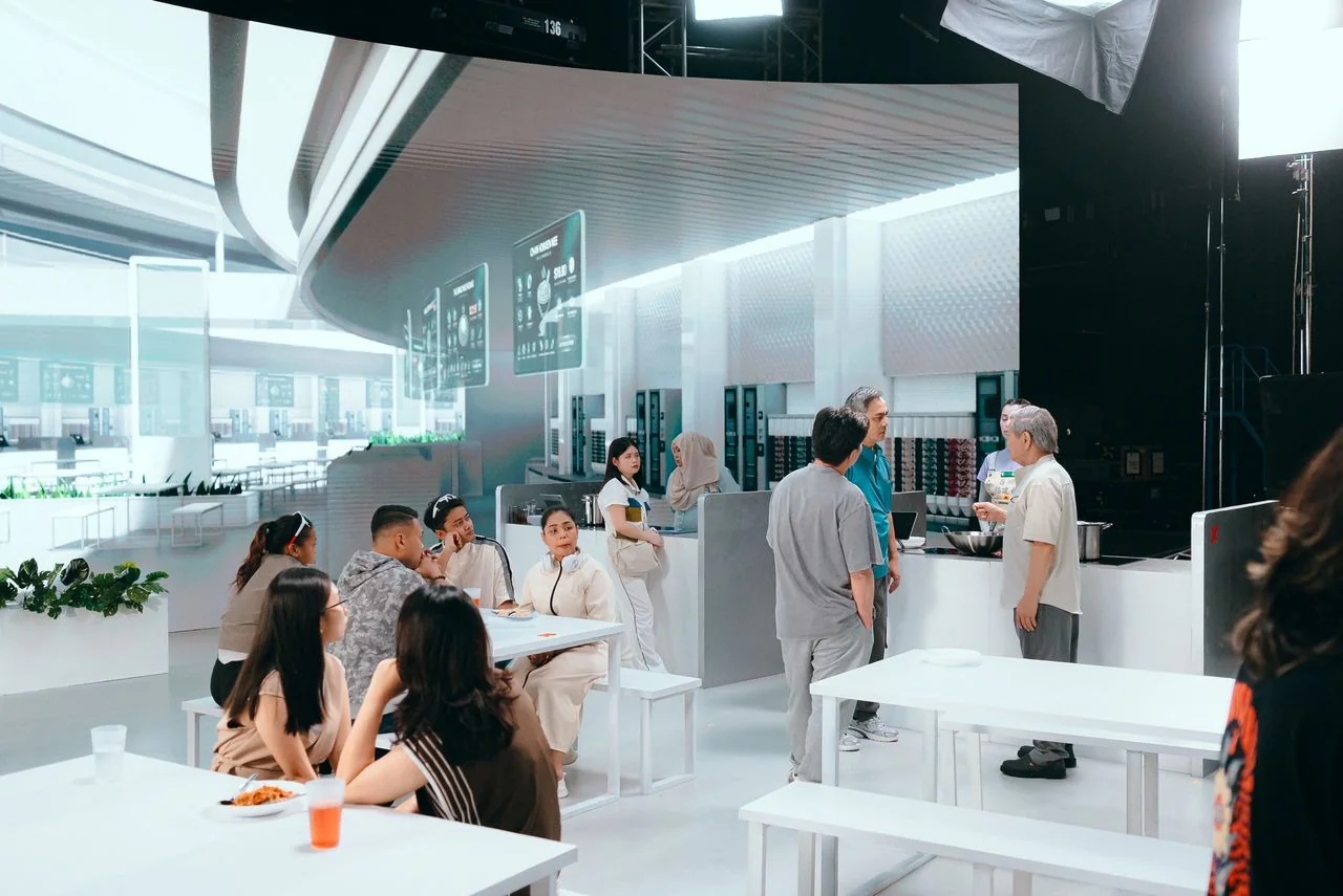 Practical white tables and foreground extras on the future hawker-centre set, with the LED stage visible beyond.